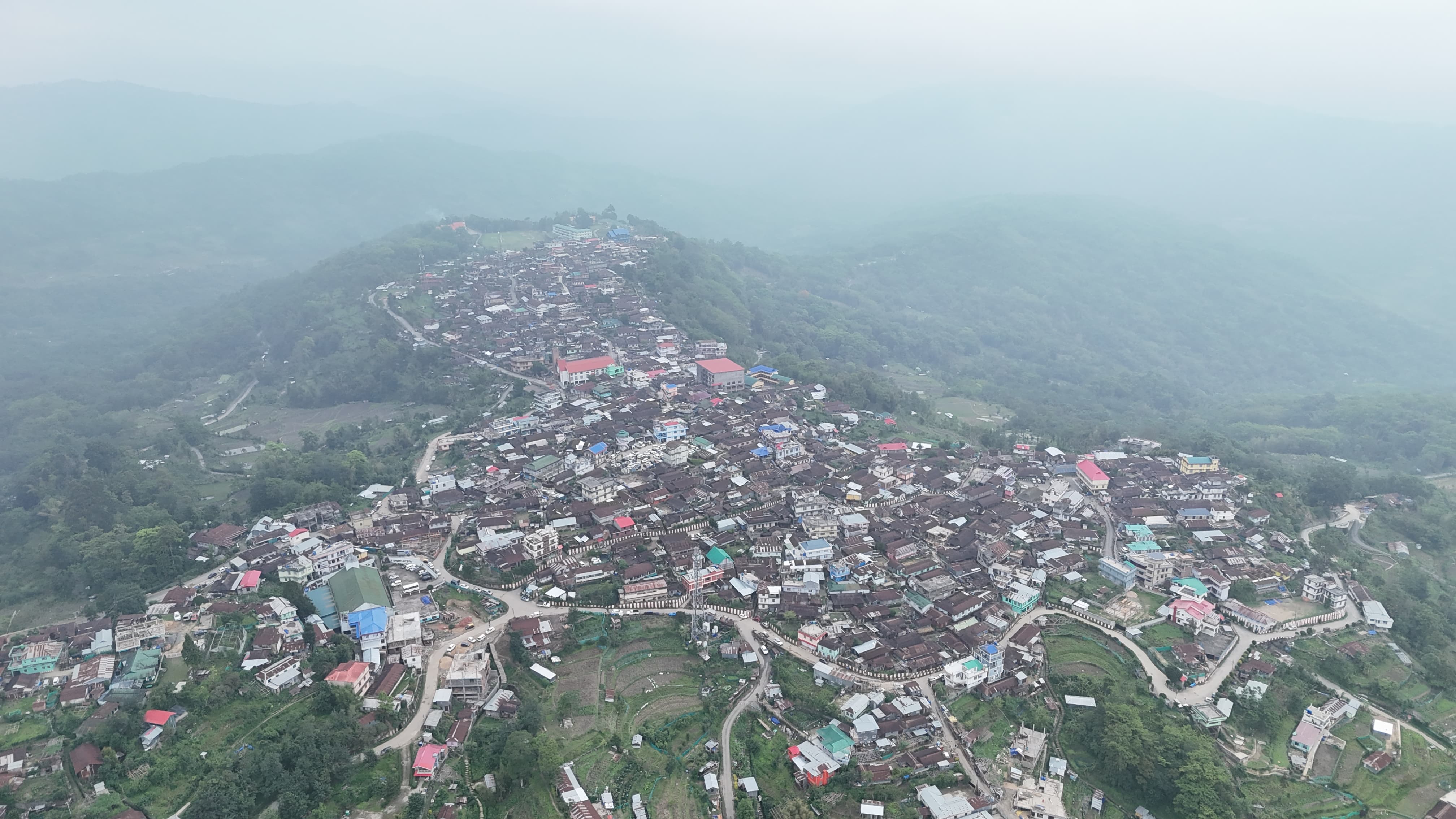 Wide aerial view of Viswema village stretched along the mountain ridge with valleys falling away on either side